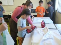 ５年生家庭科の授業の様子です。今回もボランティアの方々に来ていただき、子供たちのエプロン制作を見守っていただきました。最初にアイロンがけを行いました。まち針で留めて、アイロンをかけました。アイロンをかけた後、しつけ縫いをしました。しつけ縫いが終わった子は、ミシンで縫い始めました。